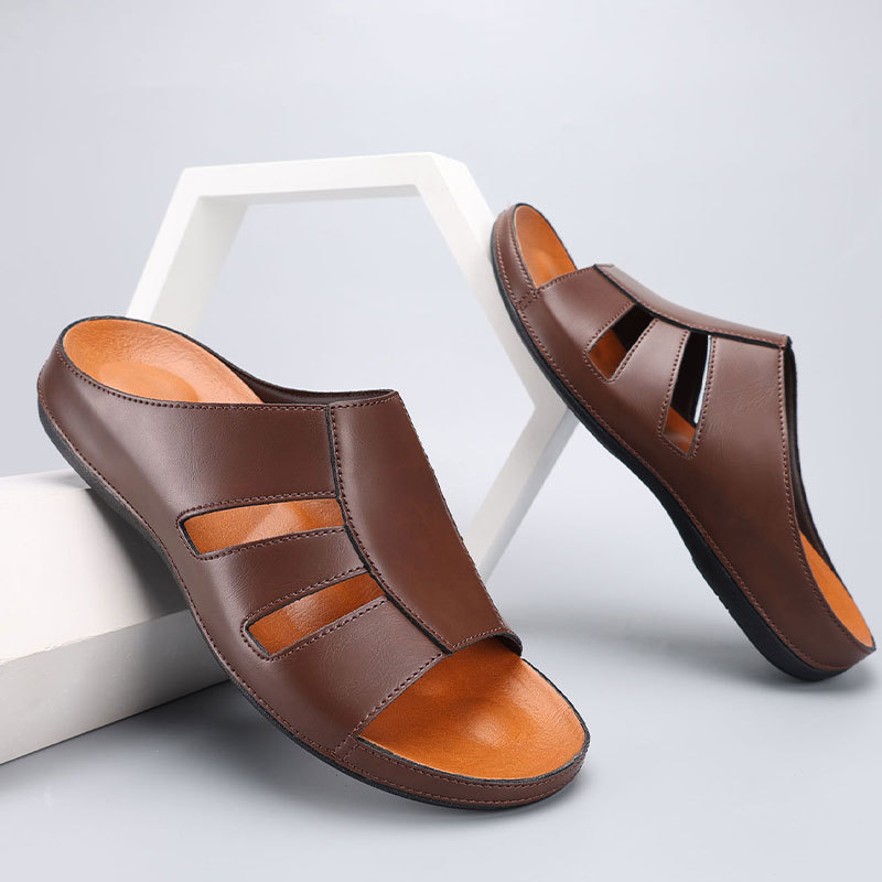 Pair of dark brown leather slip-on sandals with cutout straps and orange footbeds, styled leaning against white geometric display blocks.