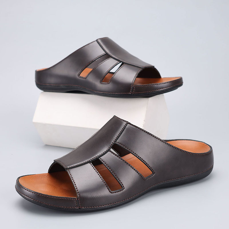 Pair of chocolate brown leather slip-on sandals with cutout straps, one shoe stacked on a white display block above the other.