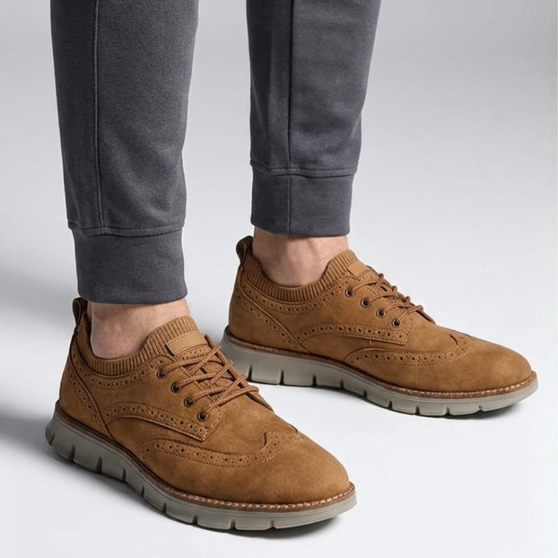 A person wearing tan suede sneakers and gray joggers, standing against a plain light background.
