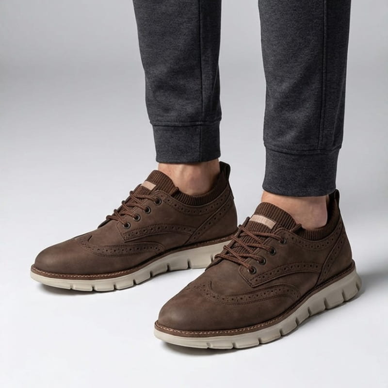 A person wearing dark brown suede sneakers and gray joggers, standing against a plain light background.