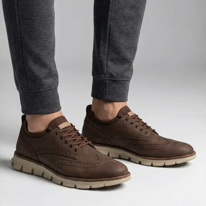 Close angled view of a person's feet wearing dark brown suede sneakers and gray joggers in a studio setting.