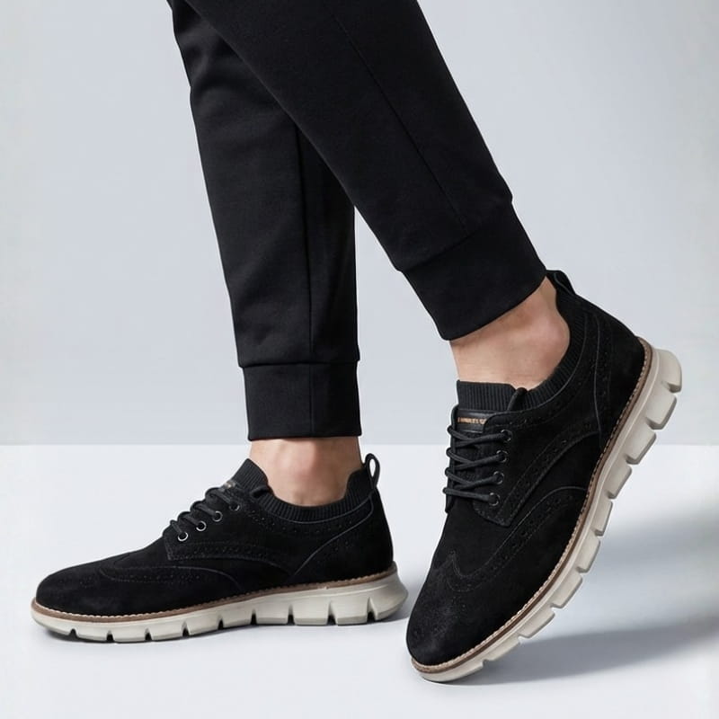 A person wearing black suede sneakers and black joggers, standing against a plain light background.