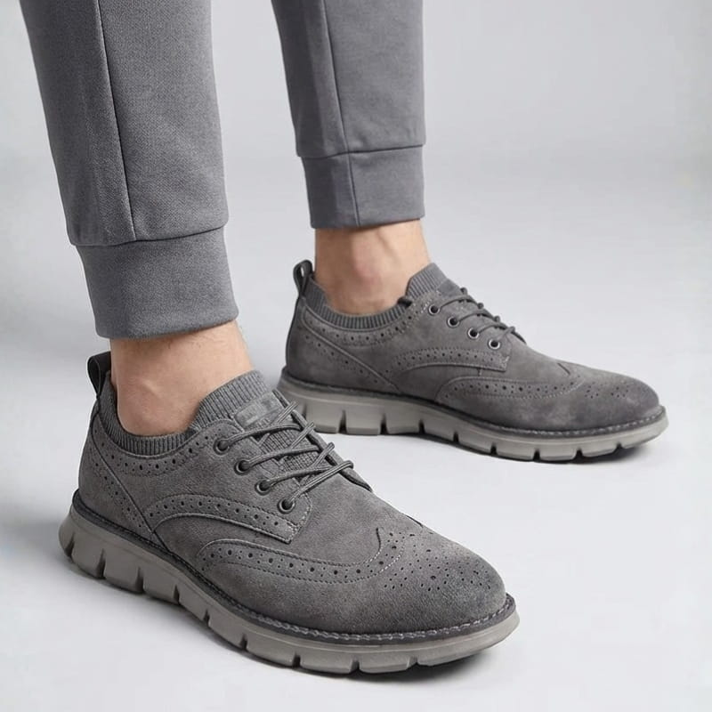 A person wearing gray suede sneakers and gray joggers, standing against a plain light background.