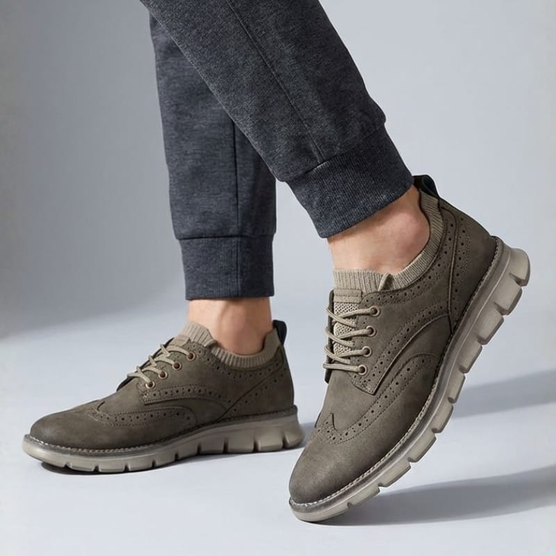 A person mid-step wearing olive suede sneakers and dark navy joggers against a plain light background.