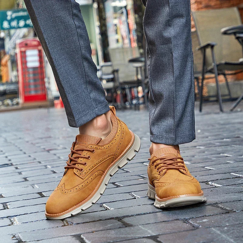 A person walking on a cobblestone street wearing tan suede sneakers and tailored gray trousers, a red phone booth visible in the background.