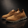 Pair of brown suede brogue-style sneakers on a reflective surface against a dark moody studio background.
