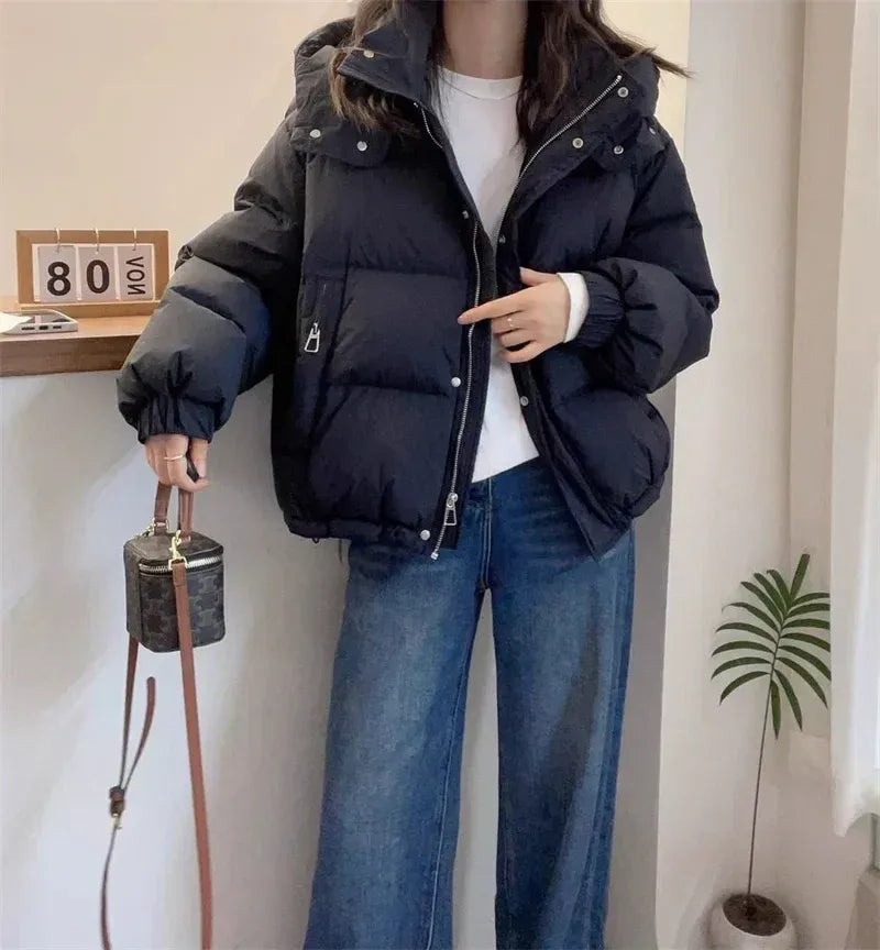 Black quilted puffer jacket with a high funnel neck, attached hood, and relaxed fit worn over a white top and jeans.