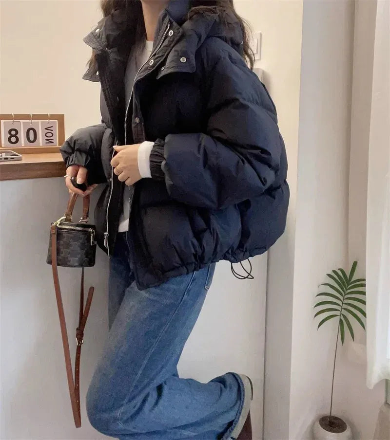 Black hooded puffer jacket with quilted insulation, high funnel neck, and relaxed fit worn with blue jeans.