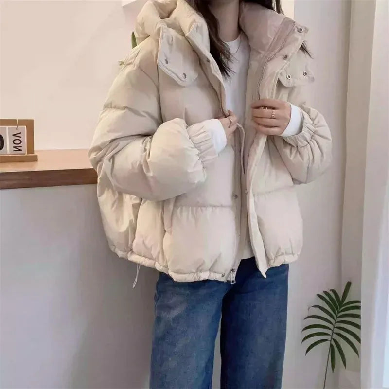 Cream hooded puffer jacket with a high funnel neck, quilted insulation, and a relaxed fit worn over a white top.