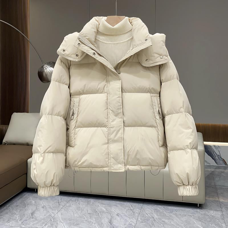 Cream hooded puffer jacket with quilted insulation, high funnel neck, and zip pockets, layered over a ribbed knit sweater.