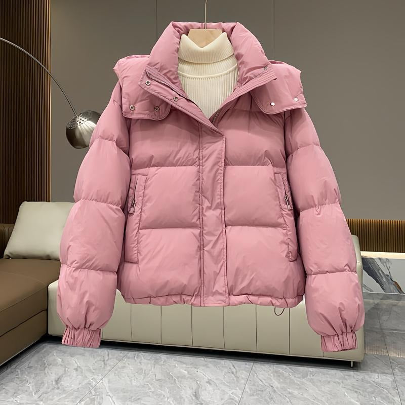 Dusty pink hooded puffer jacket with quilted insulation, high funnel neck, and zip pockets, layered over a cream sweater.