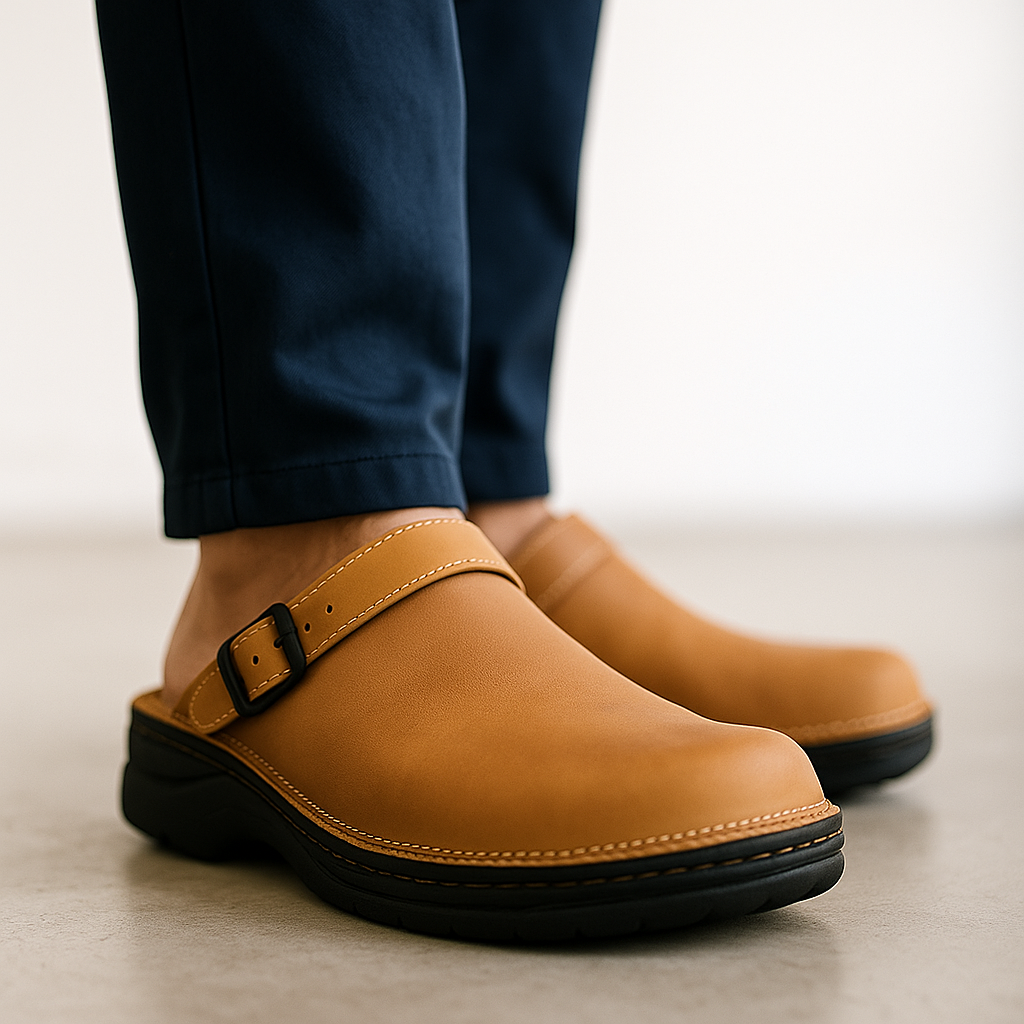 Tan leather slip-on clogs featuring an adjustable buckle strap and supportive cushioned outsole, paired with dark trousers for a casual everyday look.