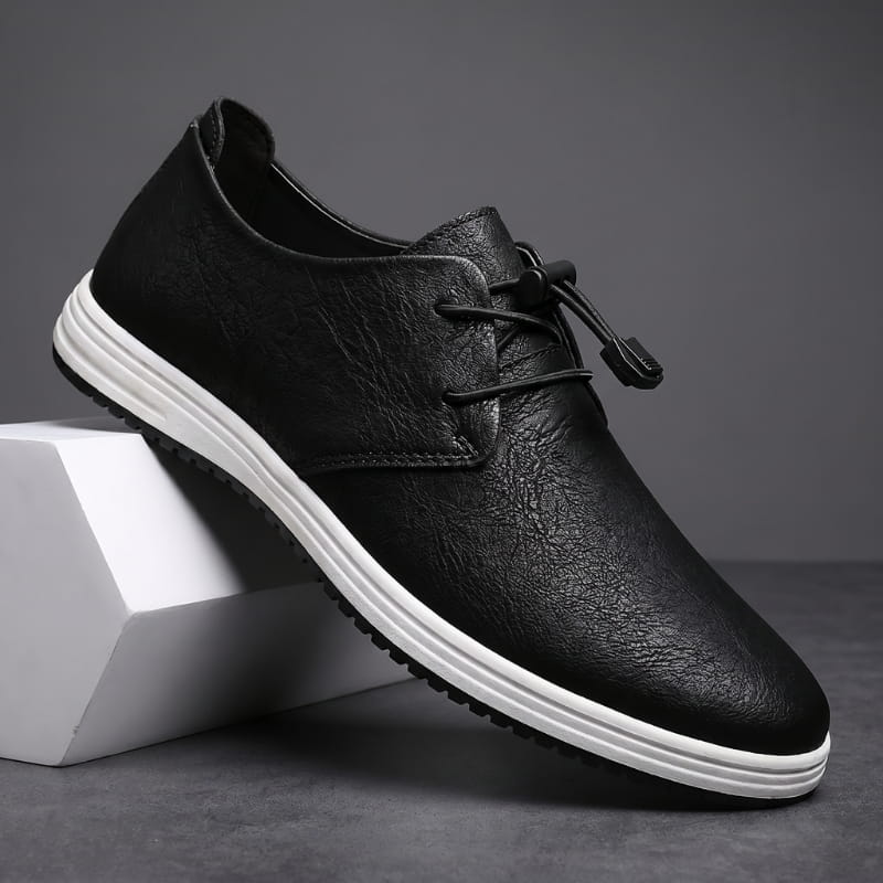 Black leather lace-up sneaker with white sole propped diagonally against a white geometric block in a studio setting