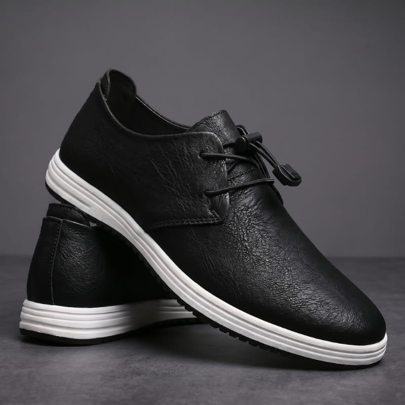 Pair of black leather lace-up sneakers with white soles stacked at an angle on a gray studio background