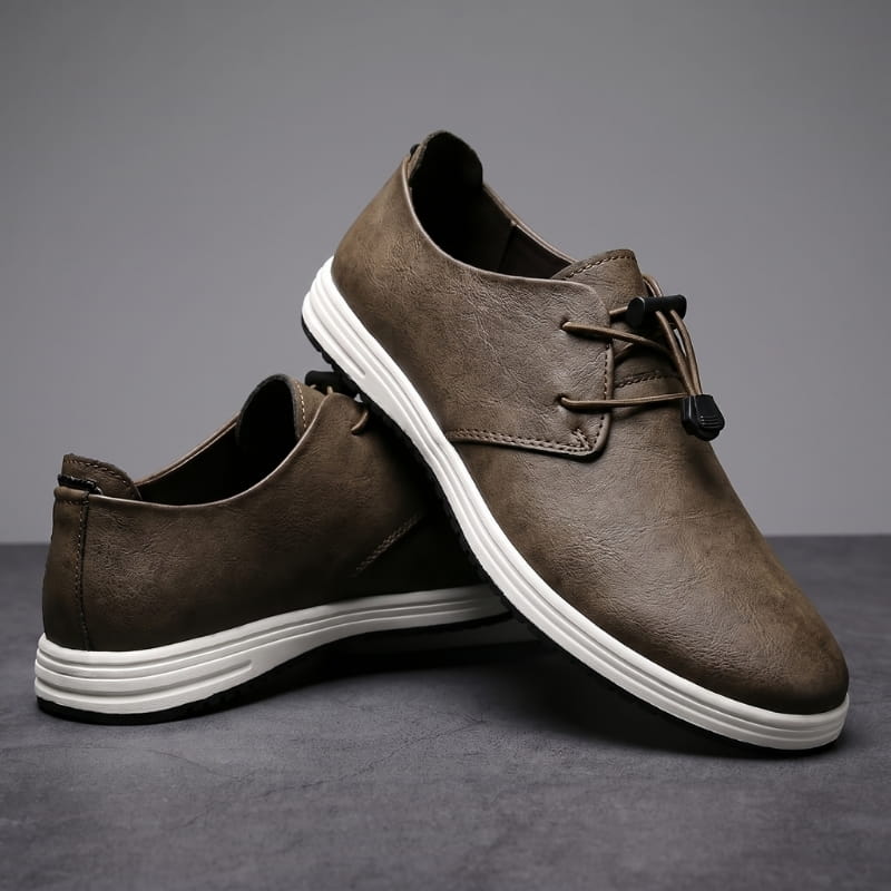 Pair of brown leather lace-up sneakers with white soles stacked at an angle on a gray studio background