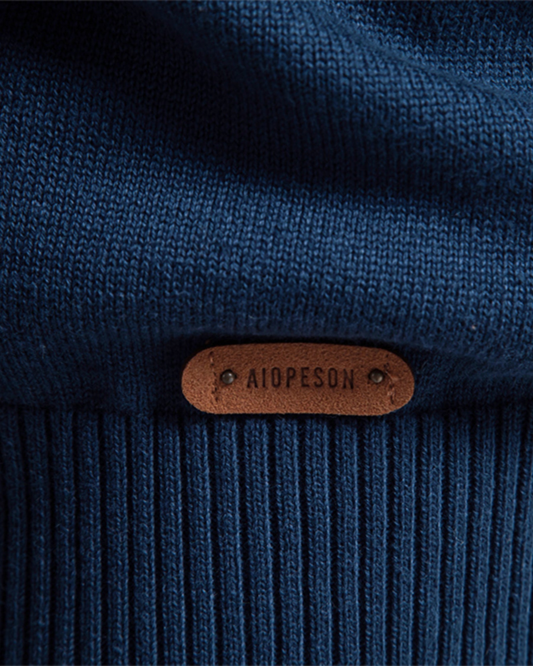 Close-up of the blue knit sweater ribbed hem featuring a brown leather logo patch.