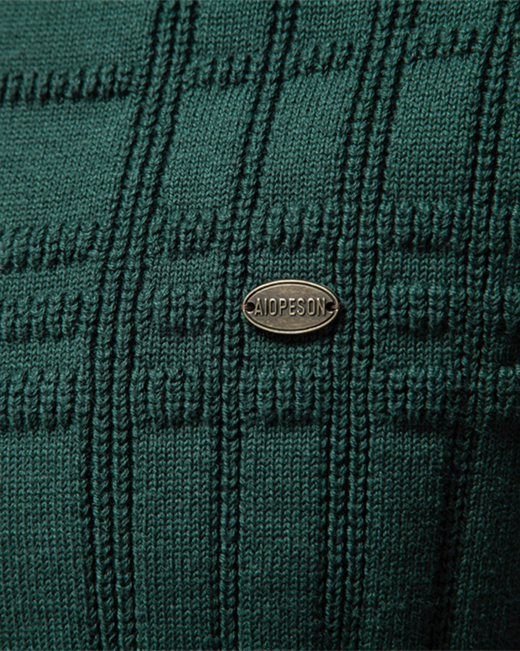 Close-up of the green textured knit sweater chest featuring the woven pattern and decorative logo badge.