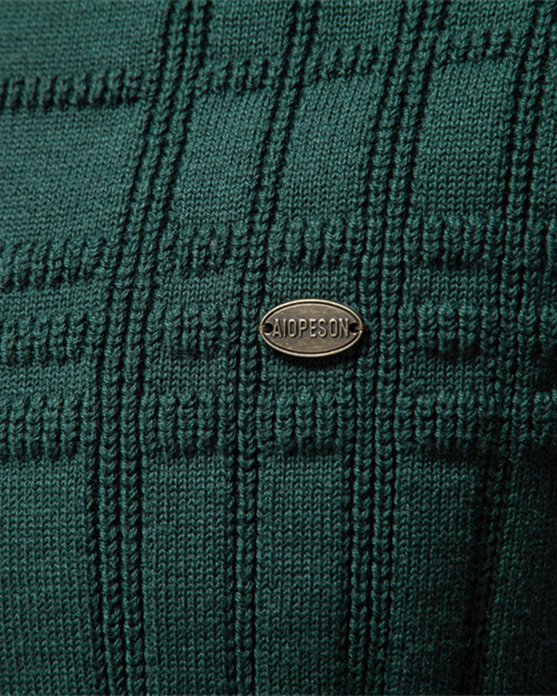 Close-up of the green textured knit sweater chest featuring the woven pattern and decorative logo badge.