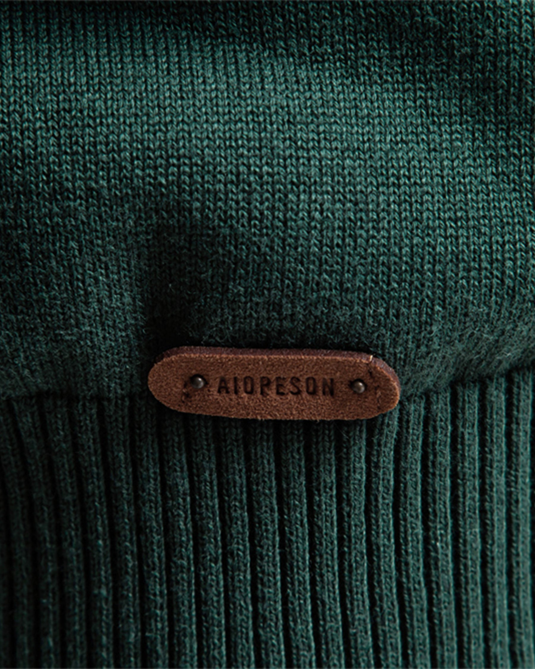 Close-up of brown leather brand patch on forest green knit sweater cuff