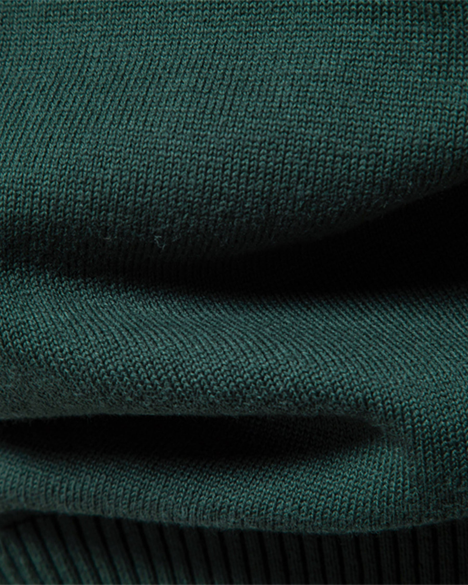 Close-up of forest green ribbed knit sweater texture and side seam