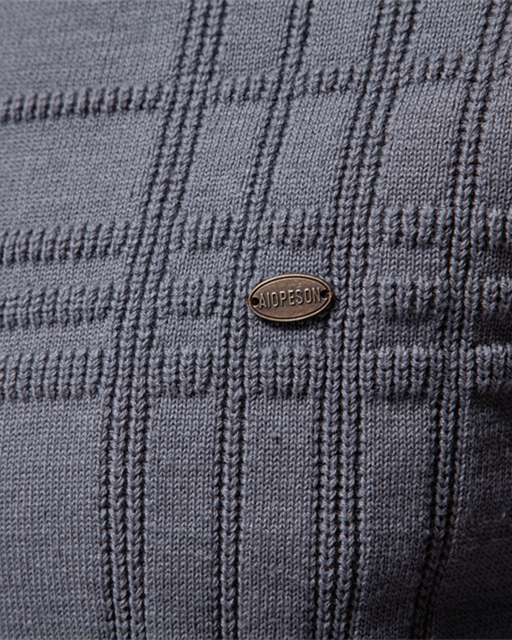 Close-up of the gray textured knit sweater chest featuring the woven pattern and decorative logo badge.