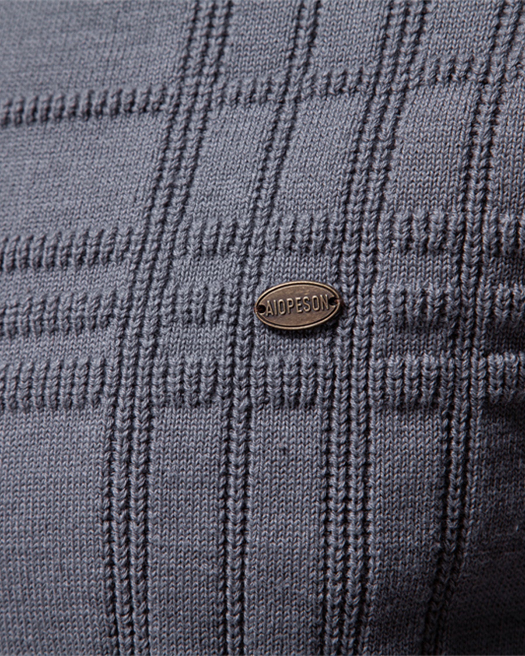 Close-up of the gray textured knit sweater chest featuring the woven pattern and decorative logo badge.