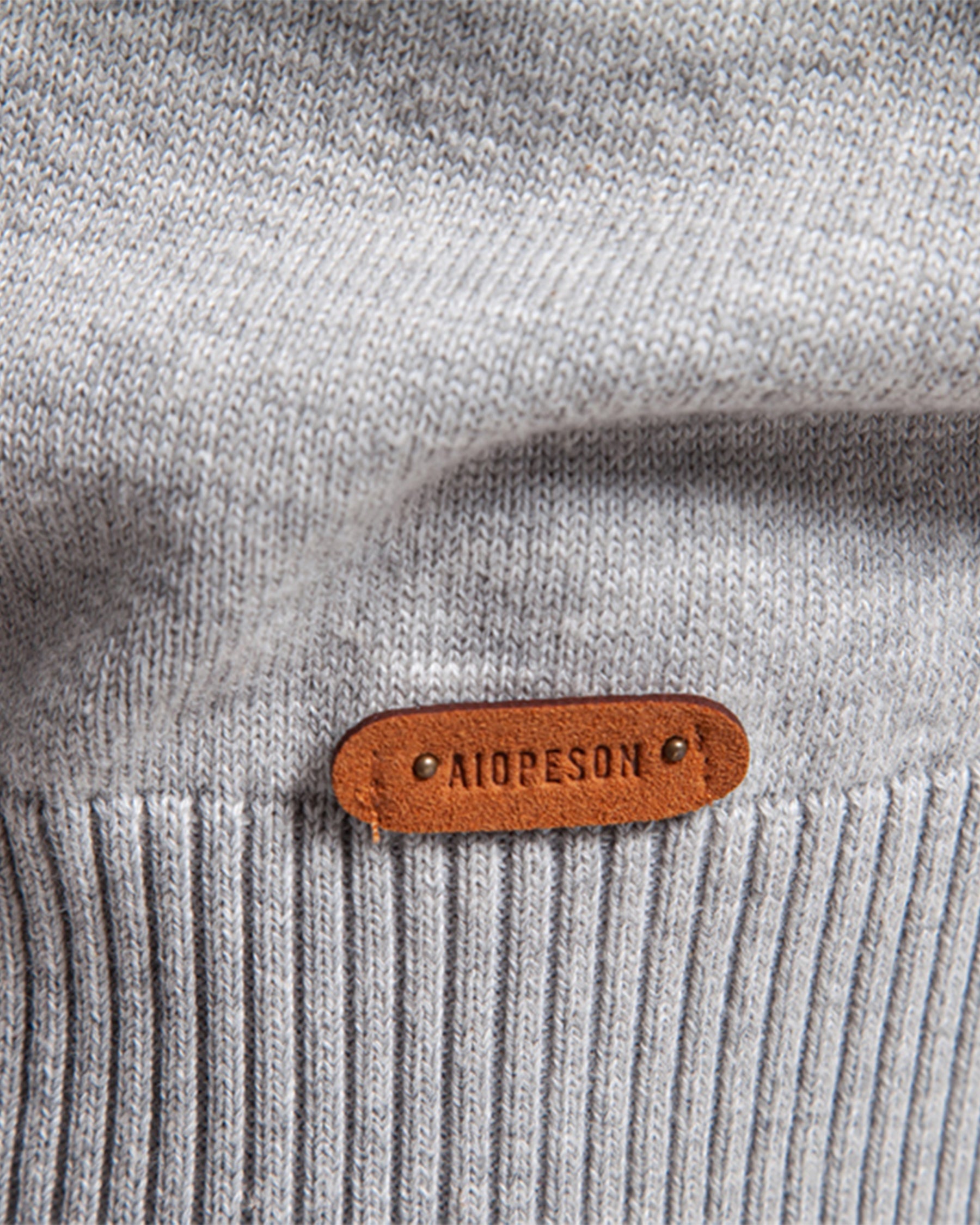 Close-up of brown leather brand patch on light grey knit sweater cuff