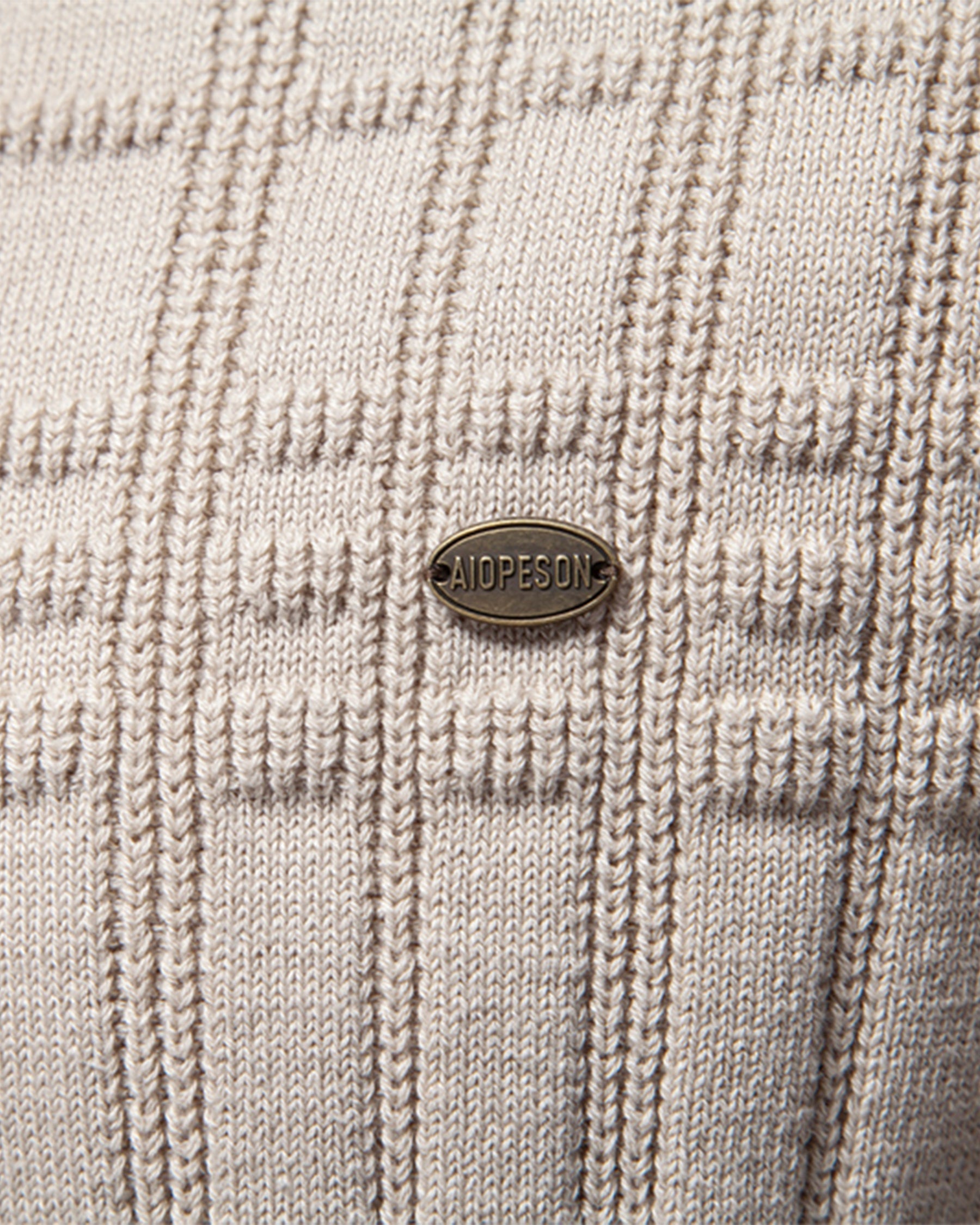 Close-up of beige knit sweater textured grid pattern with woven button detail