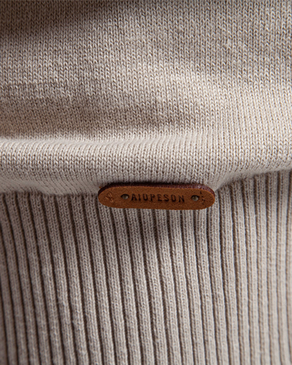 Close-up of tan leather brand patch on beige knit sweater