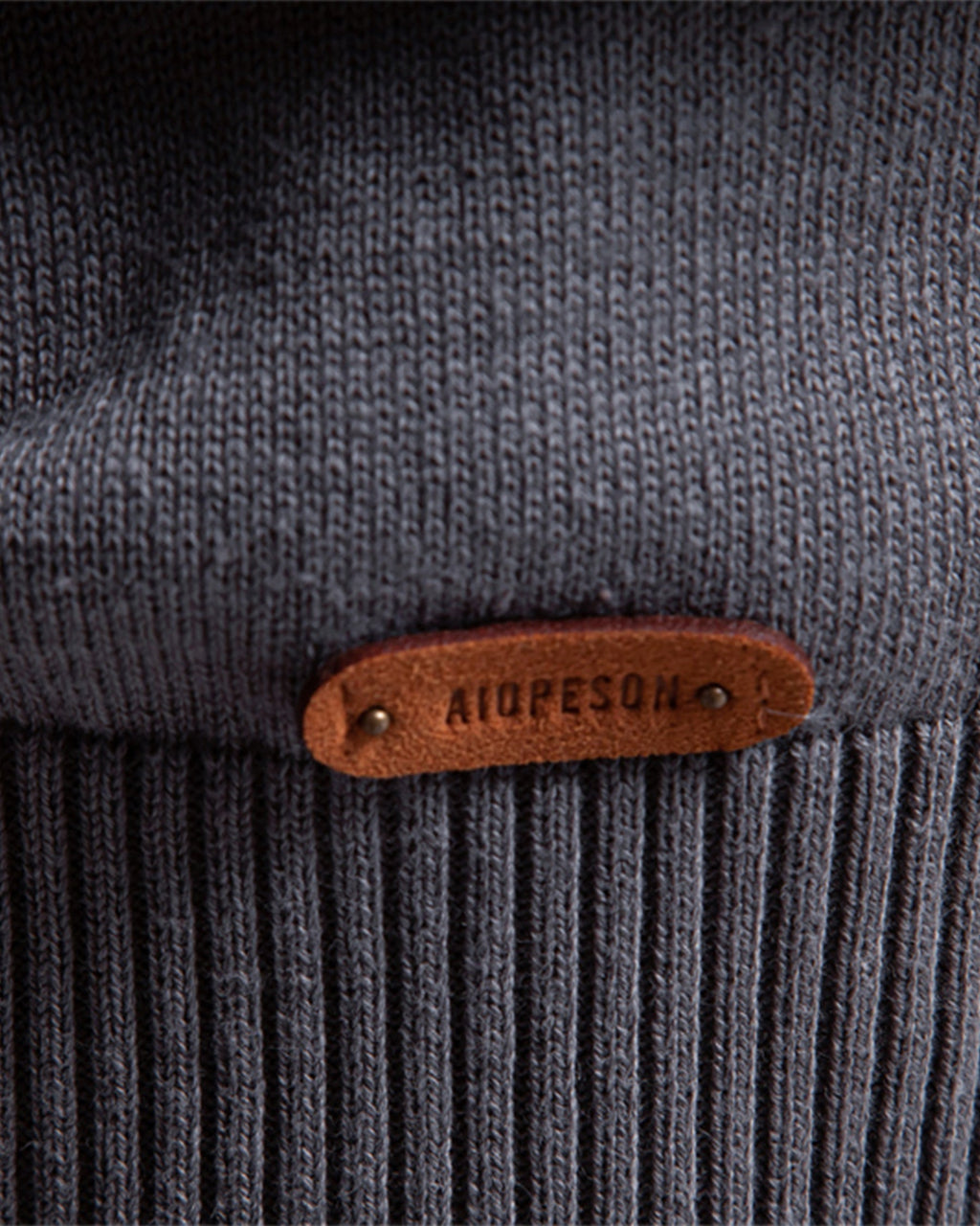 Close-up of the gray knit sweater ribbed hem featuring a brown leather logo patch.