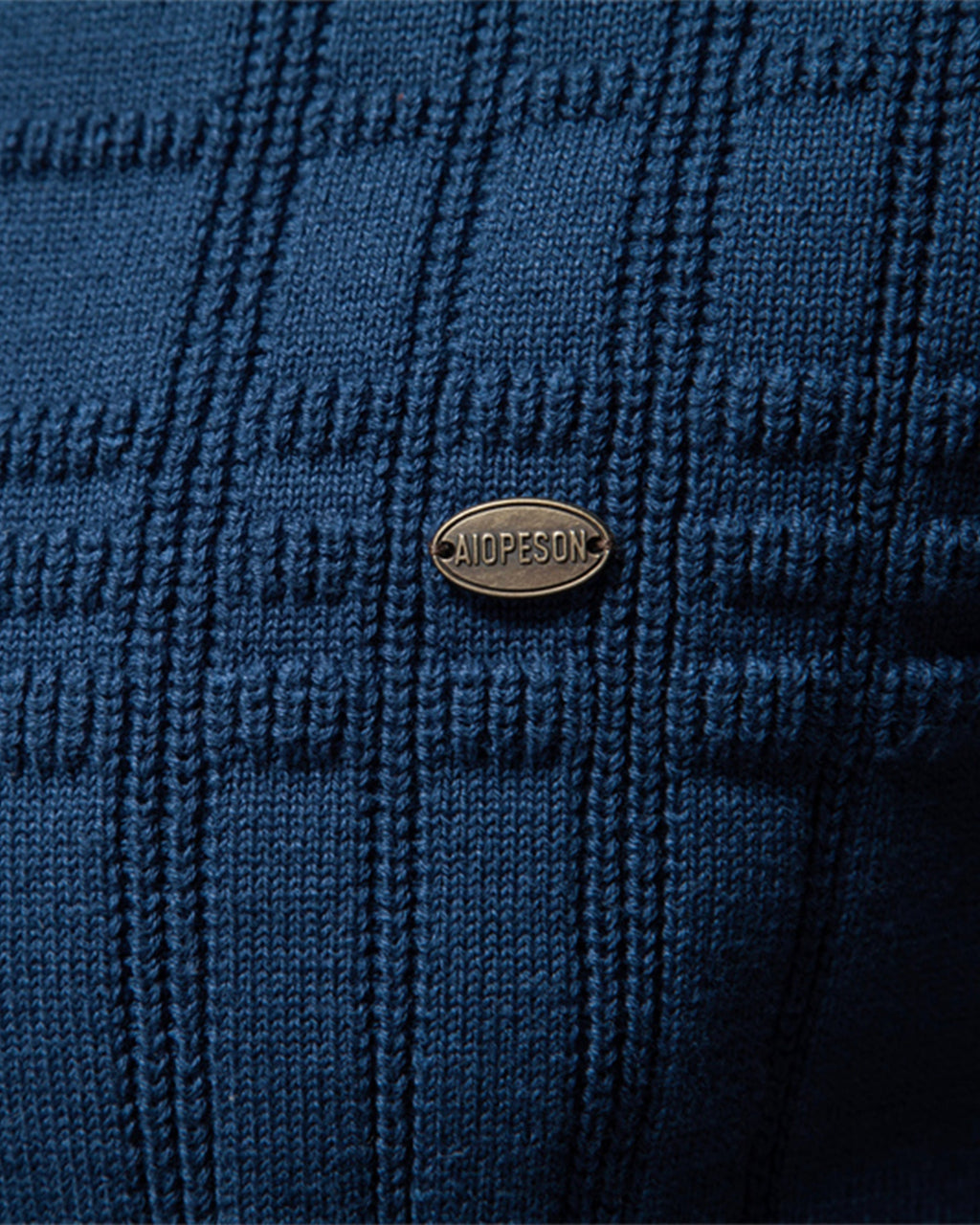 Close-up of the blue textured knit sweater chest featuring the woven pattern and decorative logo badge.