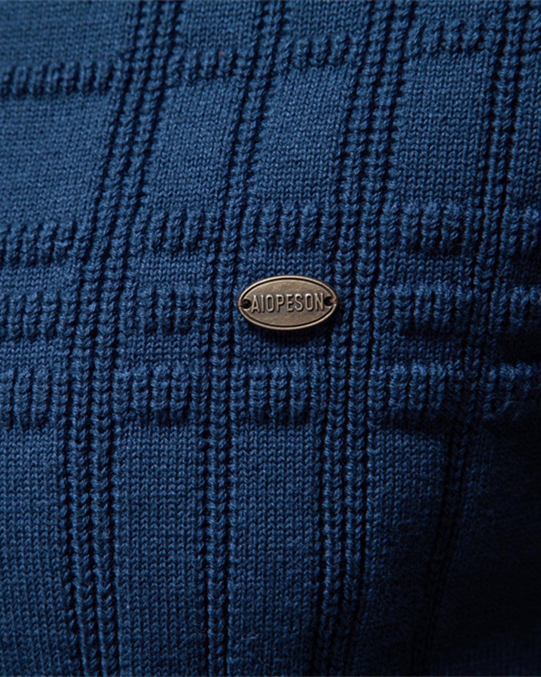 Close-up of the blue textured knit sweater chest featuring the woven pattern and decorative logo badge.