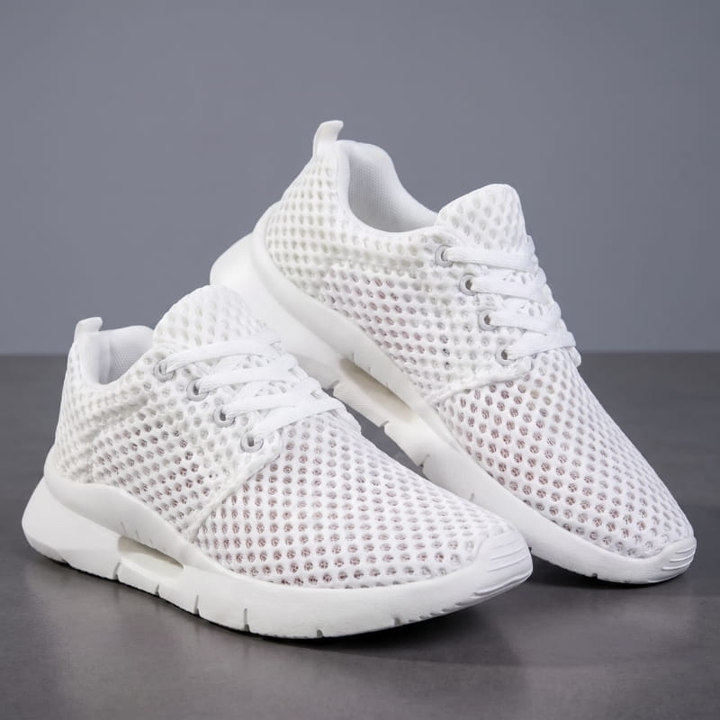 Pair of white mesh sneakers with cushioned soles stacked at an angle on a gray studio background