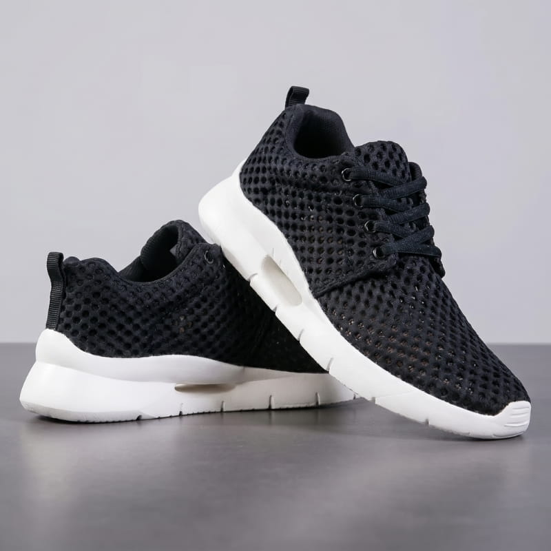 Pair of black mesh sneakers with white cushioned soles stacked at an angle on a gray studio background