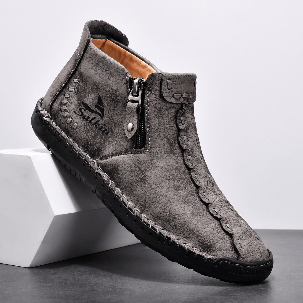 Single gray suede Javier high-top shoe with side zipper and hand-stitched trim, angled on a white block against a studio backdrop