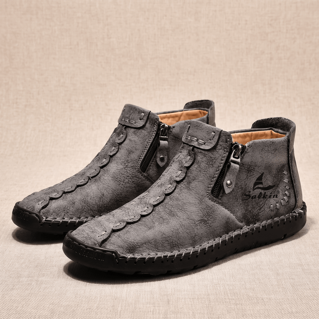Pair of gray suede Javier high-top shoes with side zippers and orange lining, resting on a beige fabric backdrop