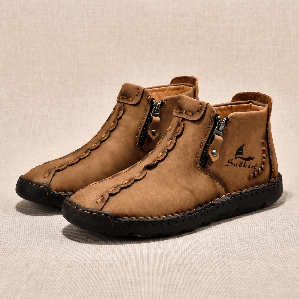 Pair of tan leather Javier high-top shoes with side zippers and hand-stitched detailing on beige backdrop