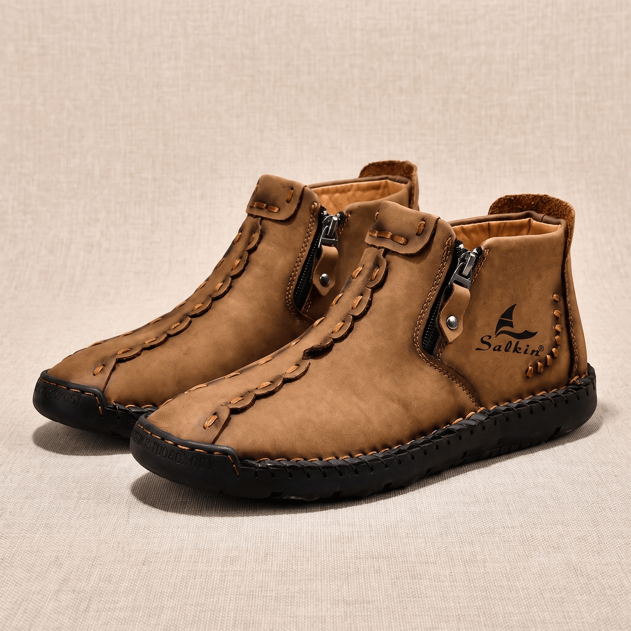 Pair of tan leather Javier high-top shoes with side zippers and hand-stitched detailing on beige backdrop