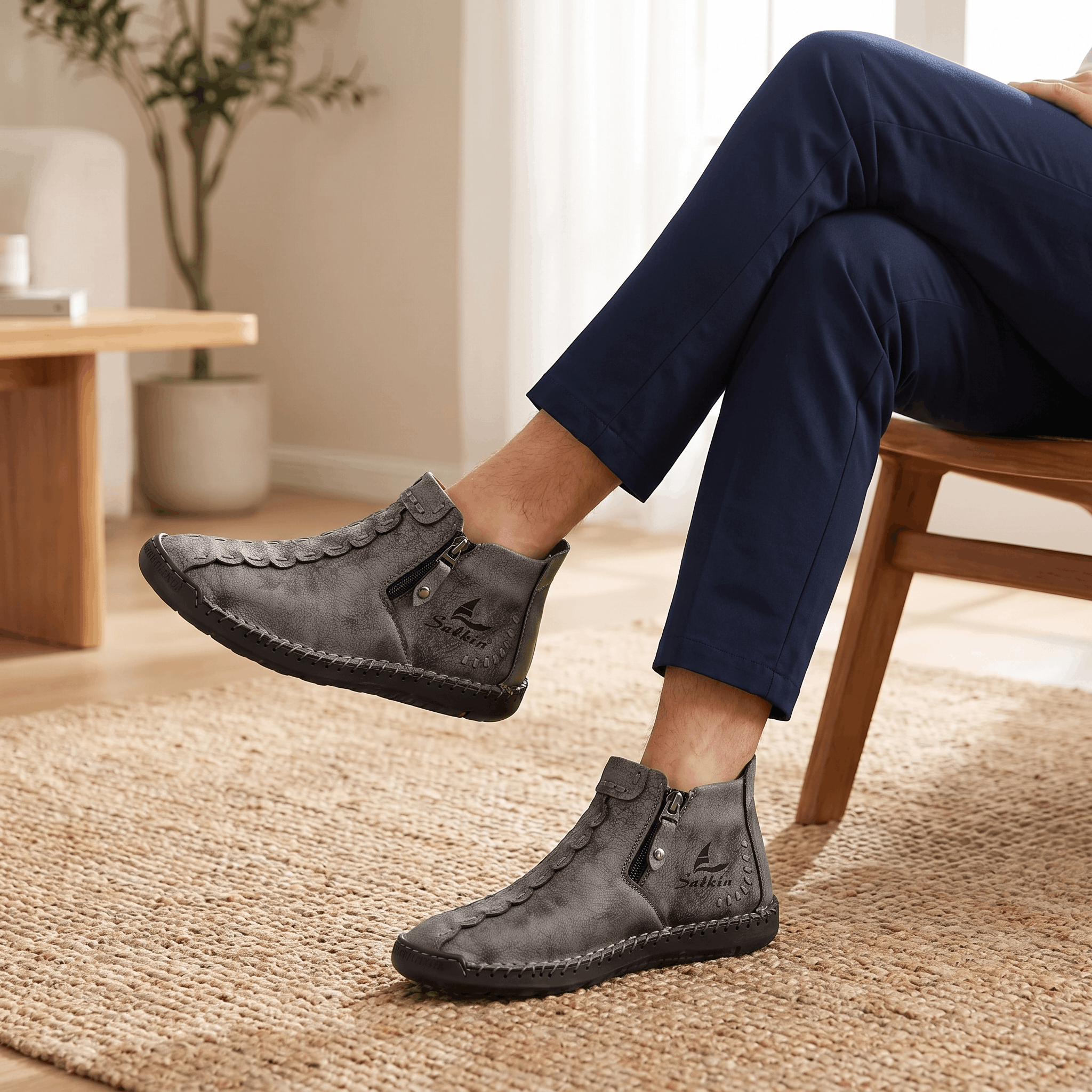 Close-up of legs extended wearing navy trousers and gray suede Javier high-top zip shoes on a jute rug near a wooden bench