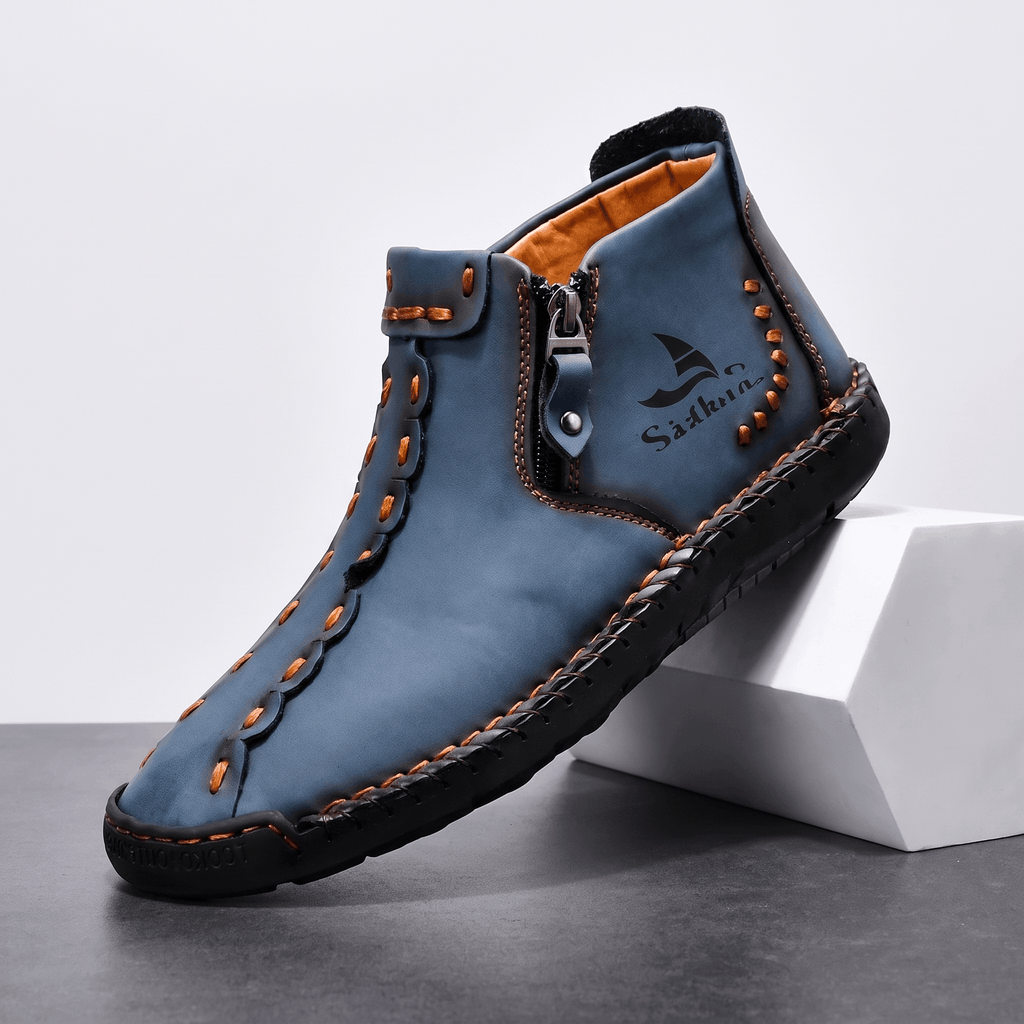 Single blue leather Javier high-top shoe with orange hand stitching and side zipper, angled on a white block against a studio backdrop