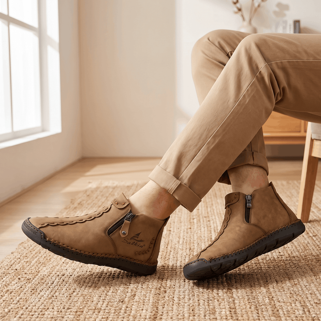Crossed legs in tan trousers wearing tan leather Javier high-top shoes with side zippers over a jute rug