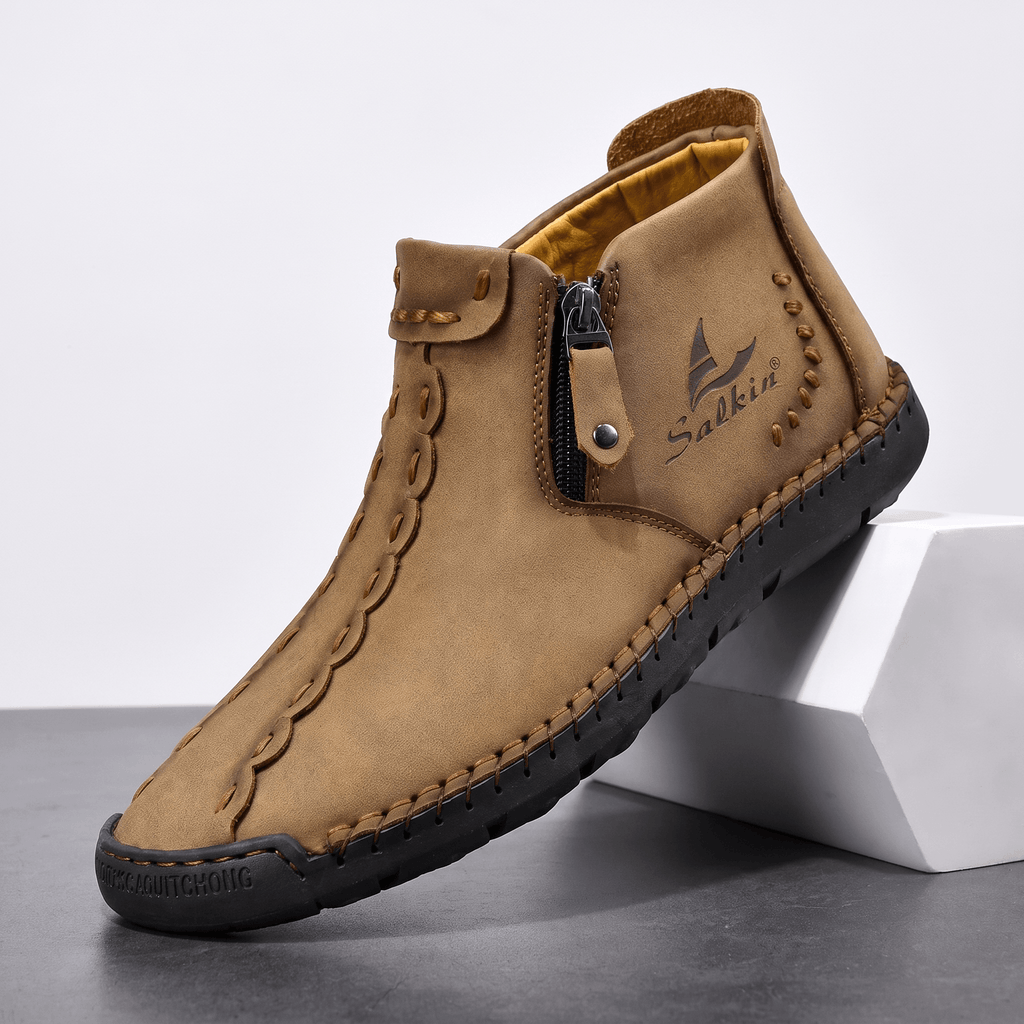 Single light brown leather Javier high-top shoe with side zipper and hand-stitched detailing, propped against a white block in studio setting