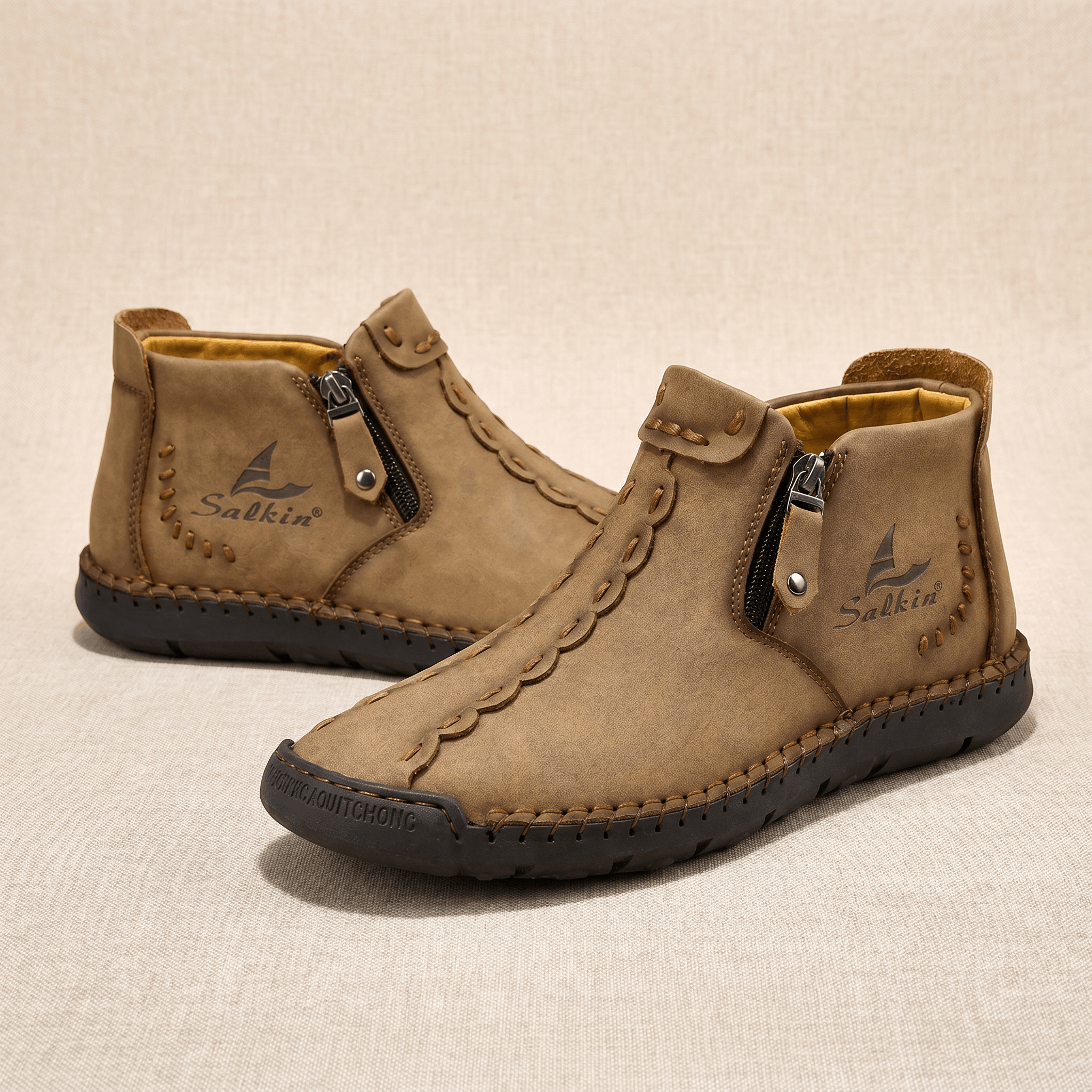 Pair of light brown leather Javier high-top shoes with side zippers and hand-stitched detailing on beige backdrop