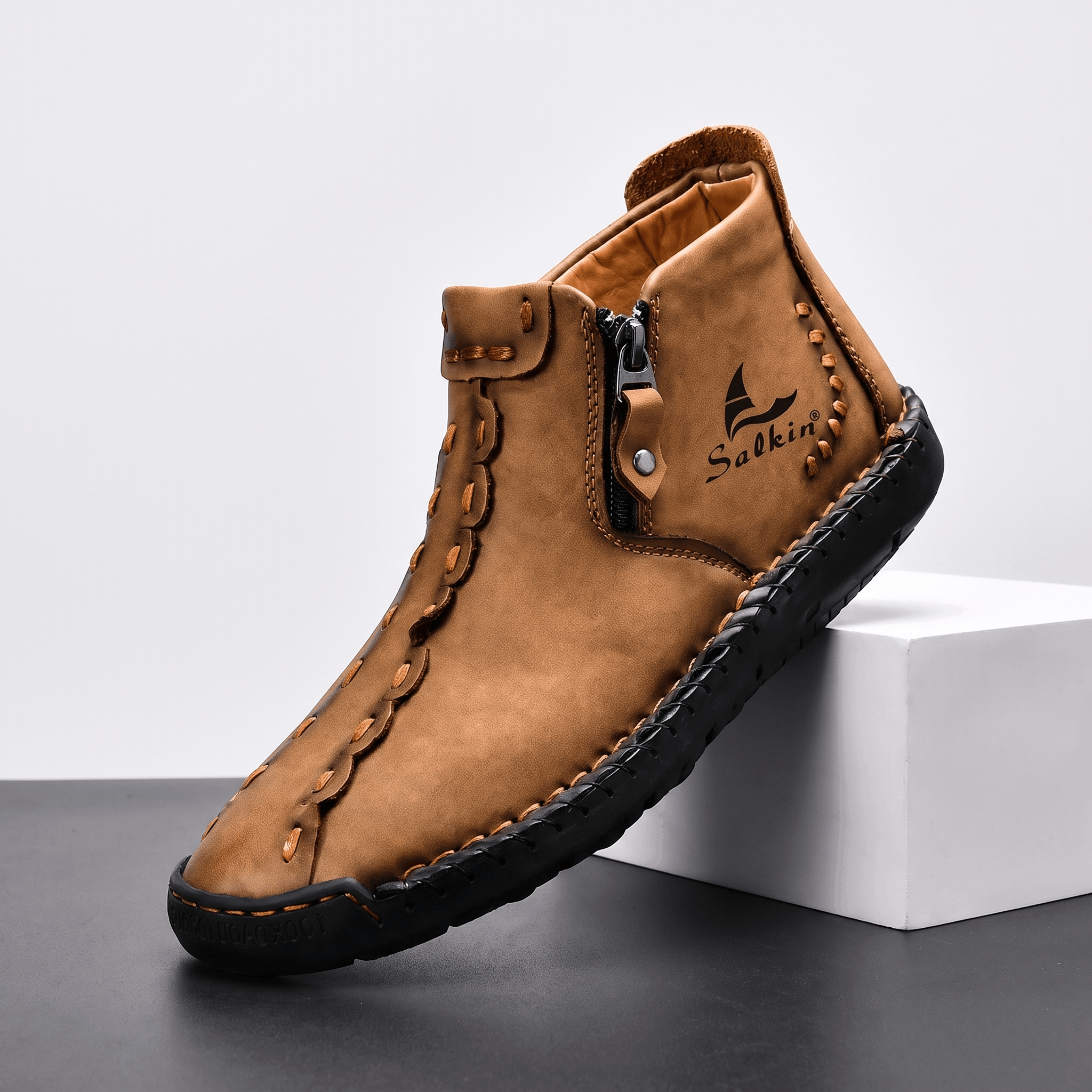Single tan leather Javier high-top shoe with side zipper and hand-stitched detailing, propped against a white block in studio setting