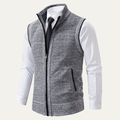 Men's gray knit zip-up sweater vest with a stand collar, sleeveless design, ribbed hem, and zip pockets layered over a white dress shirt and black tie.