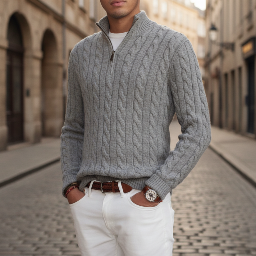 Light gray cable knit half-zip sweater with a stand collar and ribbed cuffs, styled with white trousers on a cobblestone street.