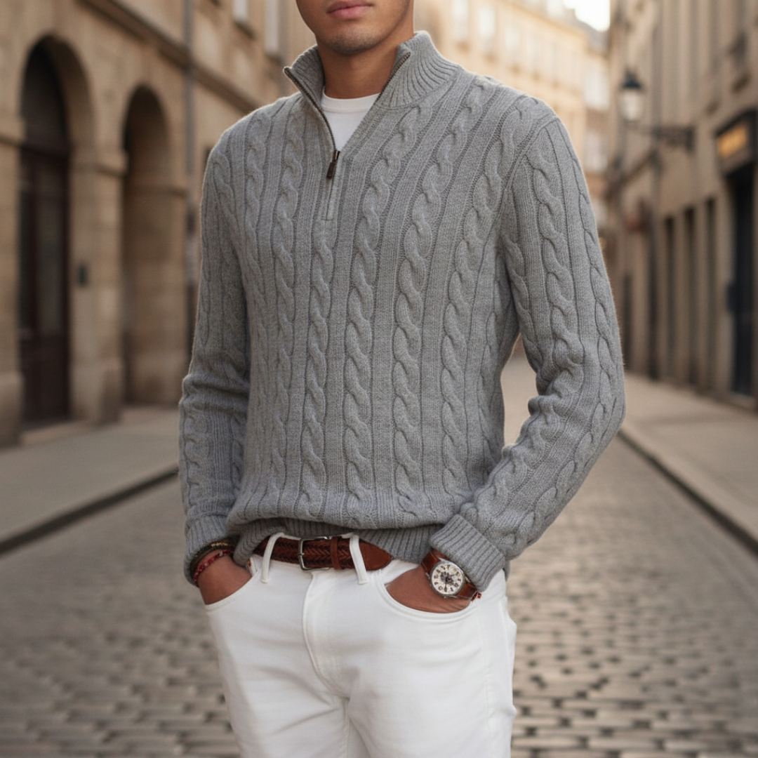 Light gray cable knit half-zip sweater with a stand collar and ribbed cuffs, styled with white trousers on a cobblestone street.