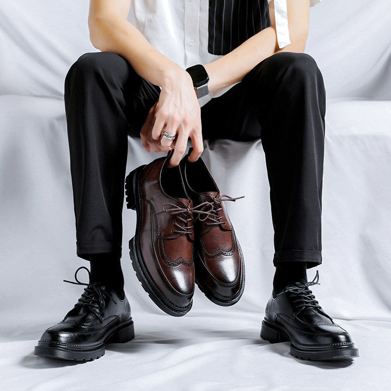 Seated man wearing black Julian brogue dress shoes on his feet while holding a brown pair of the same style in his lap