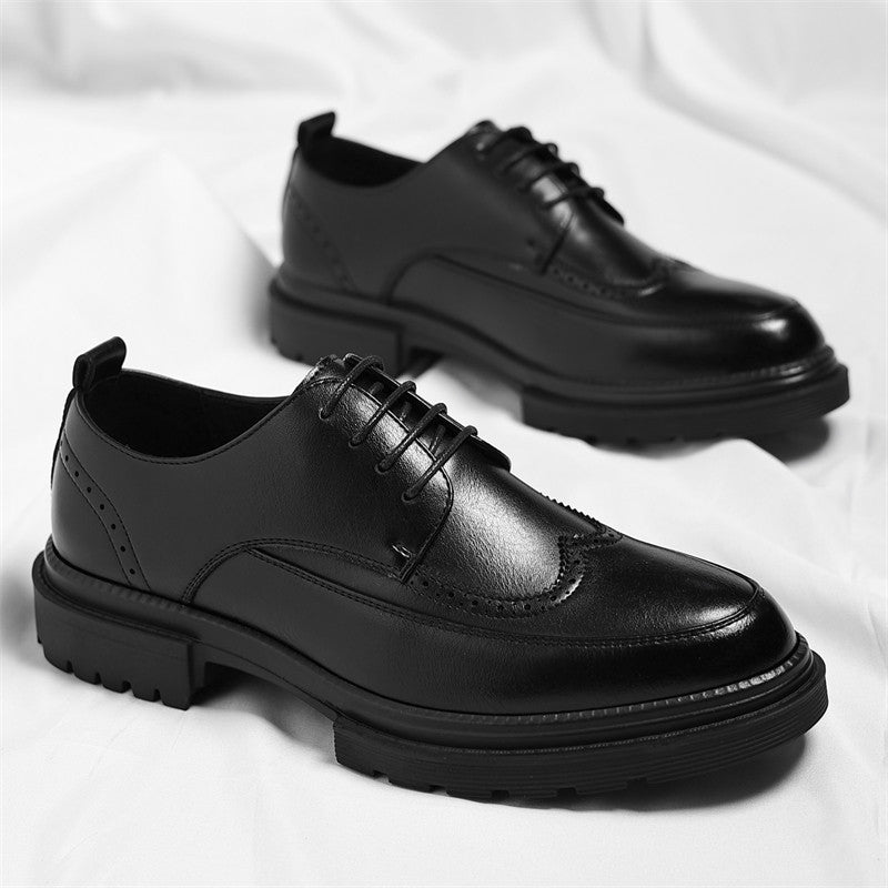Pair of black leather Julian brogue dress shoes with wingtip stitching, one propped on the other on a white fabric backdrop