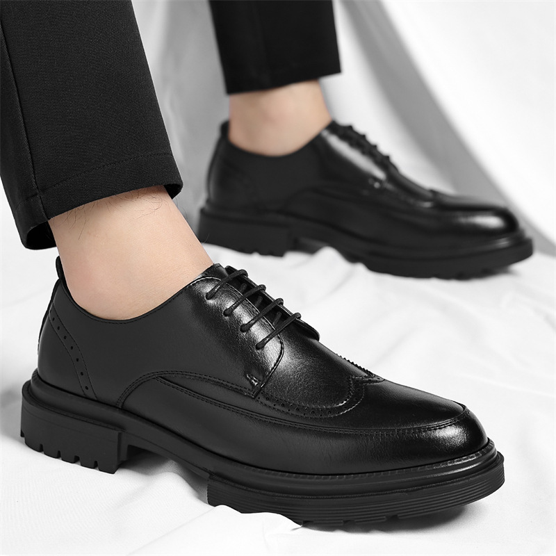 Man wearing black leather Julian brogue dress shoes with black tailored trousers, standing on a white backdrop